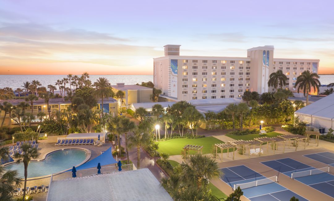 TradeWinds Island Grand Resort overlooking swimming pools, palm trees, pickleball courts, and the Gulf of Mexico at sunset on St. Pete Beach, Florida.