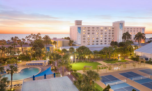 TradeWinds Island Grand Resort overlooking swimming pools, palm trees, pickleball courts, and the Gulf of Mexico at sunset on St. Pete Beach, Florida.