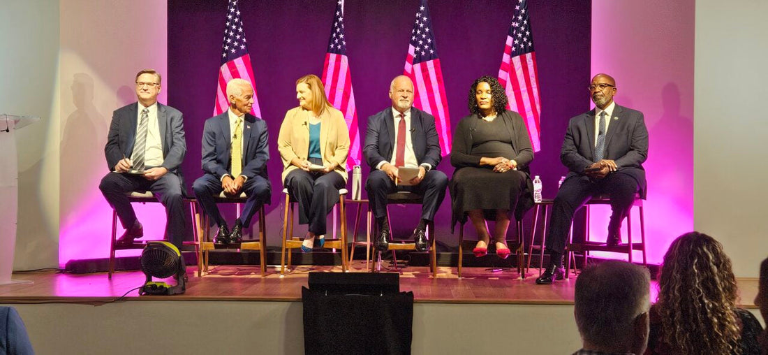 Six St. Petersburg mayoral candidates seated on stage during a 2026 mayoral forum with American flags behind them as voters weigh the future of St. Pete leadership.