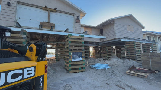 Home elevation project in progress with a raised flood-damaged Florida house supported by cribbing and steel beams during construction.