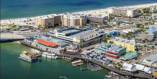 Aerial view of John’s Pass Village and Boardwalk in Madeira Beach Florida showing retail buildings, marina docks, parking garage, and Gulf beaches