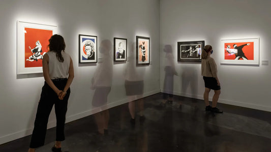 Visitors walking through a modern gallery space viewing multiple Banksy artworks on display during The Art of Banksy exhibit at the Straz Center in Tampa