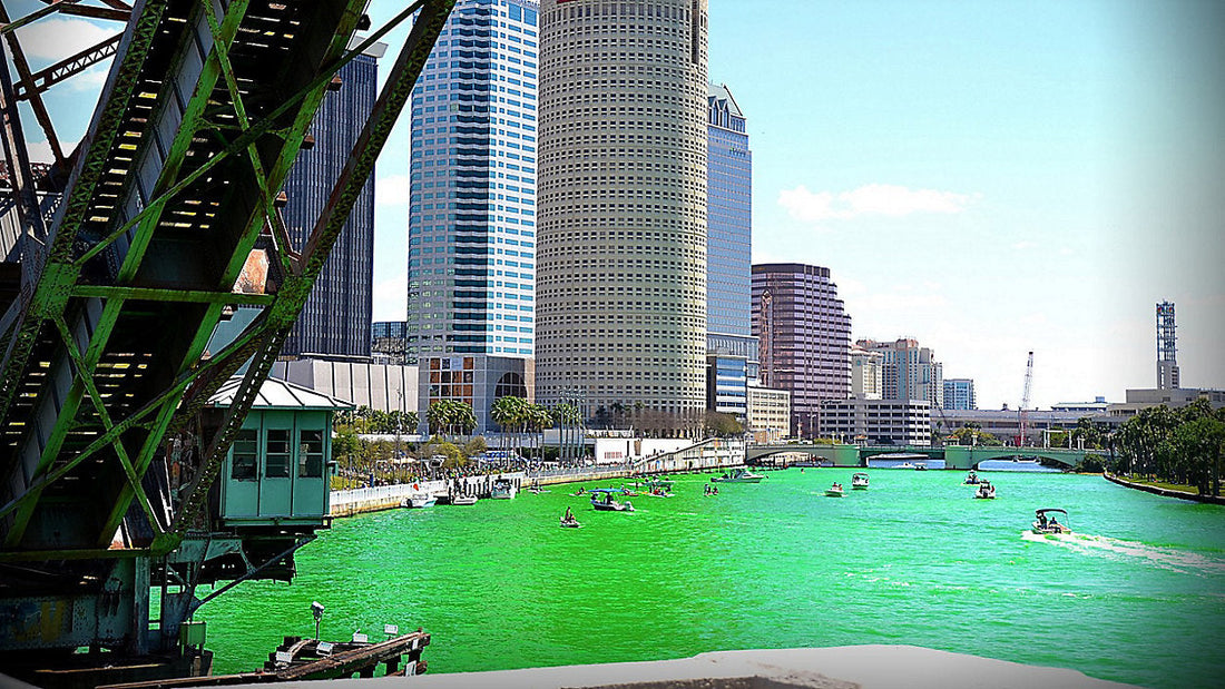 Hillsborough River turned bright green during River O’ Green Festival in downtown Tampa with boats cruising past Curtis Hixon Waterfront Park and Tampa skyline in background.