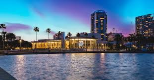 Mahaffey Theater along St. Pete waterfront skyline at dusk with downtown buildings and Tampa Bay in the foreground